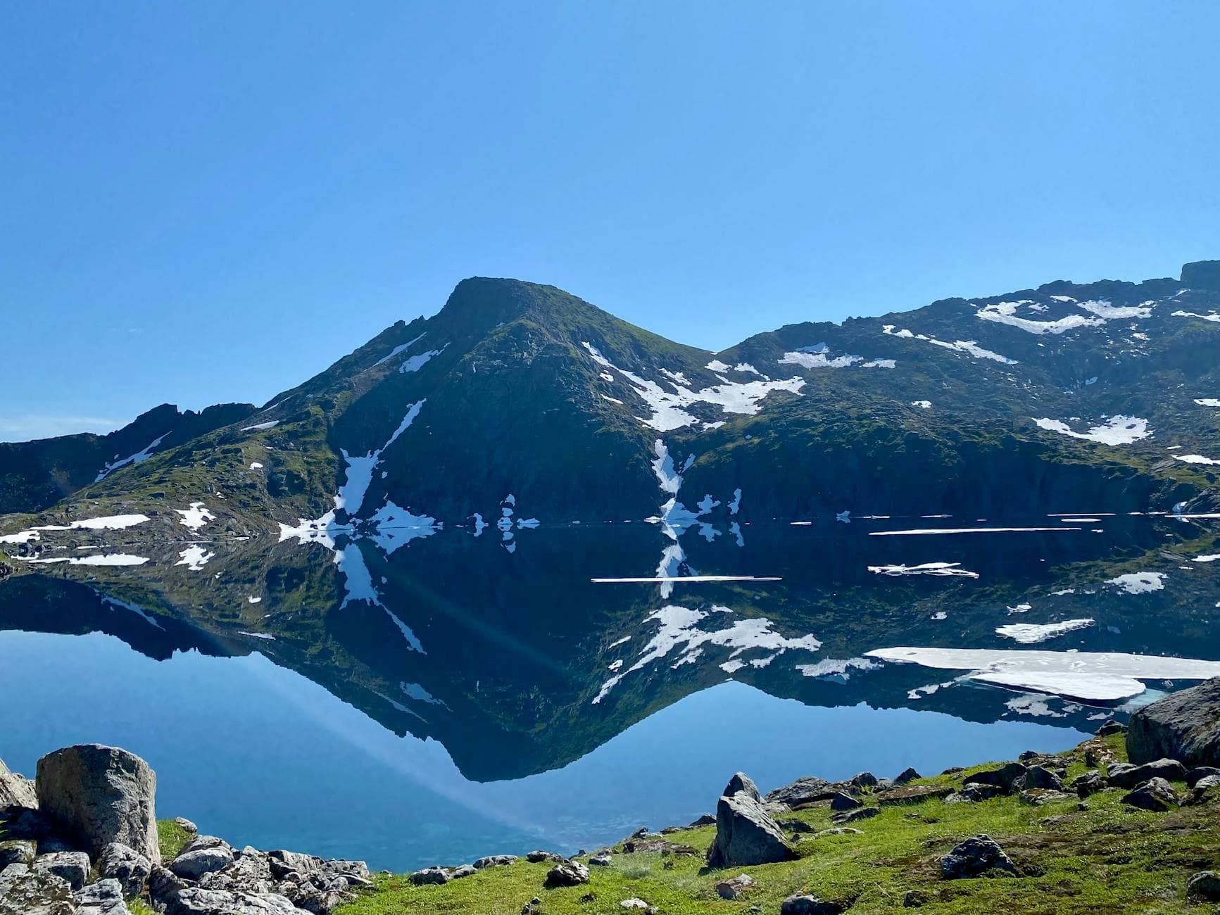 A clear mountain lake perfectly reflects a snow-capped peak under a bright blue sky.